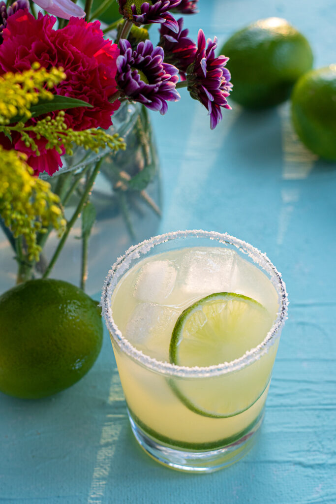 A salt rimmed glass filled to the top with ice and margarita, topped with a lime wheel.