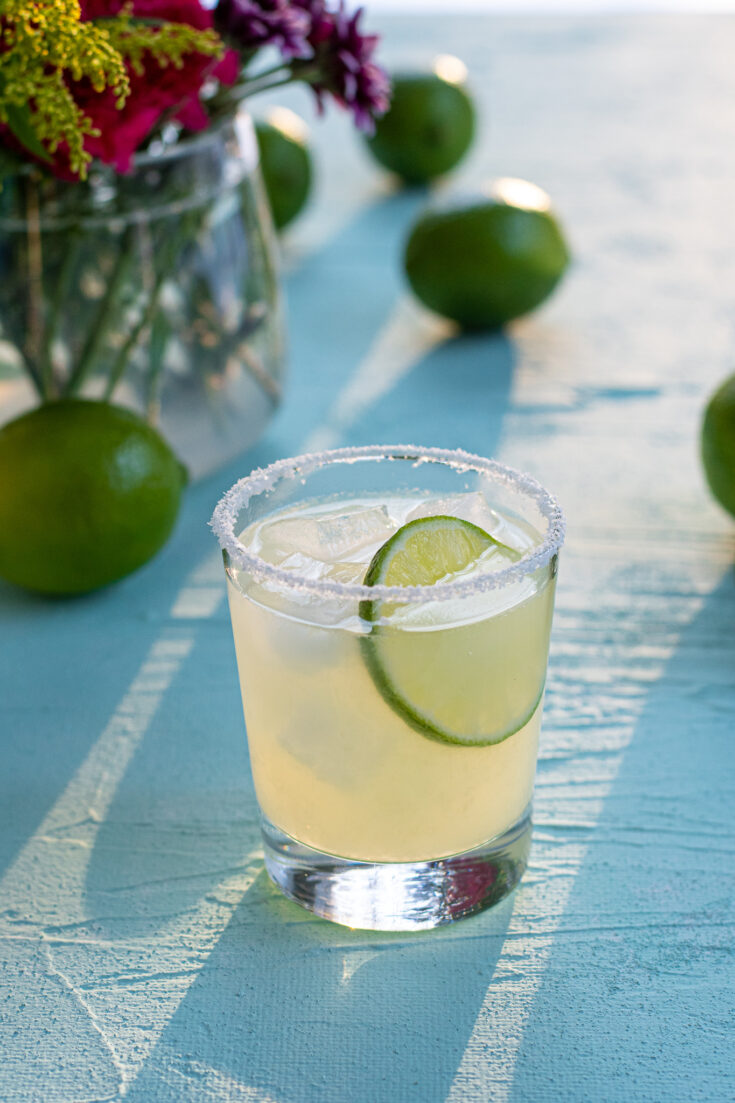 A salt rimmed margarita garnished with a lime wheel, slight pure through the drink making shadows on a blue background.