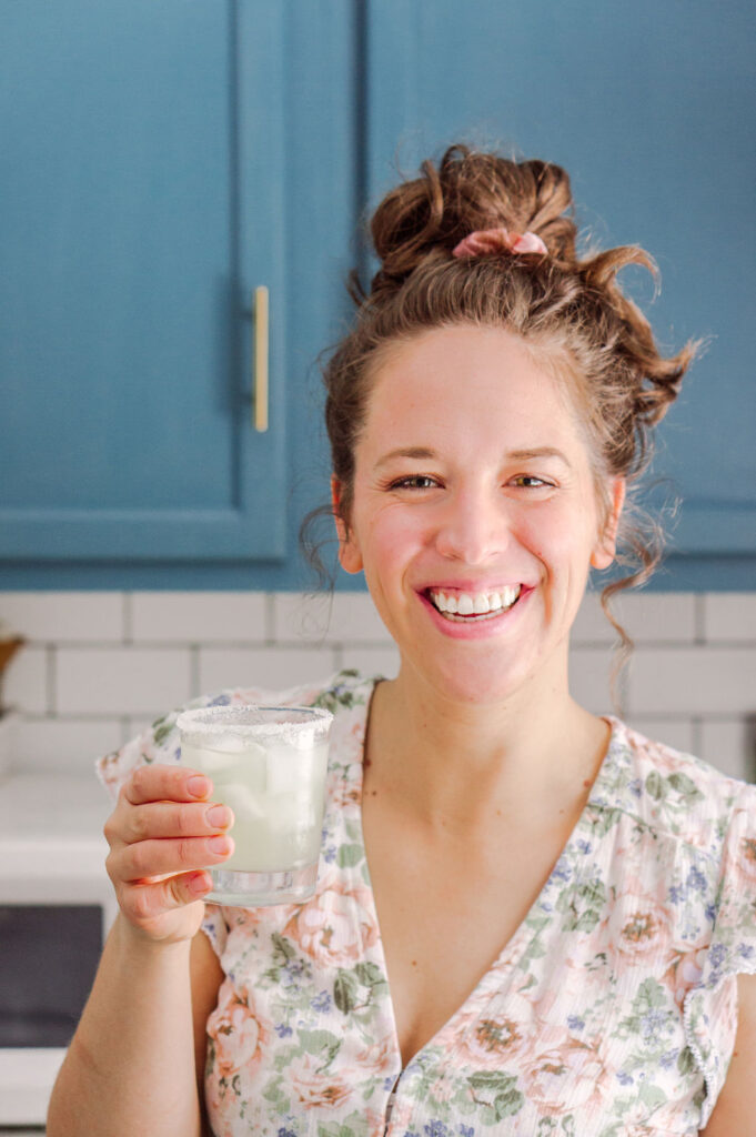 Photo of Lauren Schmidt with a large smile, margarita, and a messy bun.